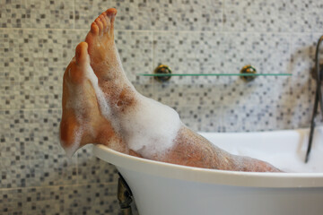 Men's feet covered with foam bubble bath in luxury bathtub with happiness and relaxing