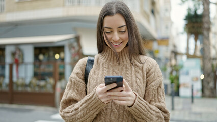 Young beautiful hispanic woman using smartphone smiling at coffee shop terrace