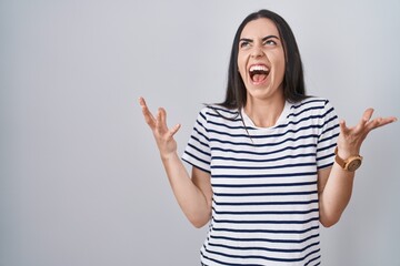 Young brunette woman wearing striped t shirt celebrating mad and crazy for success with arms raised and closed eyes screaming excited. winner concept