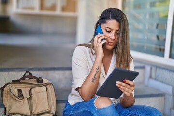 Young hispanic woman student talking on smartphone using touchpad at university