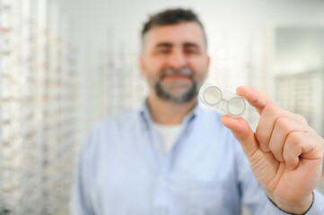 man holding contact eye lenses and container in hand, applying eye contacts from lens box