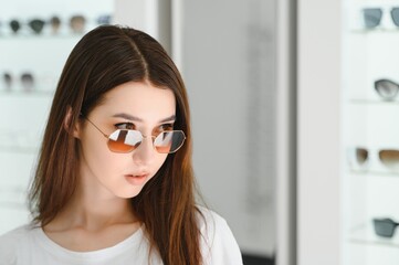 young woman chooses sunglasses for herself in an optics store