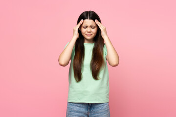 Obraz na płótnie Canvas Sad teenage girl in green t shirt touching head, headache, migraine isolated on pink background