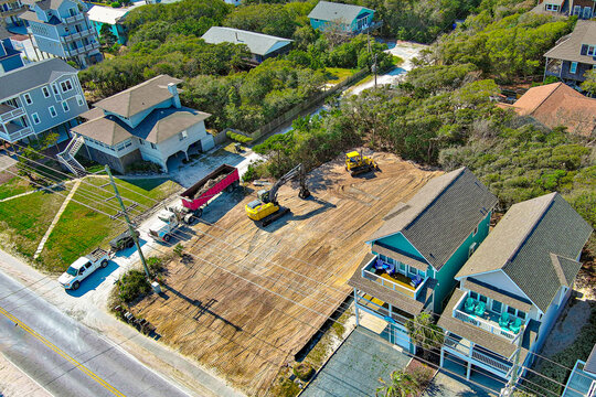 Distant top-down aerial view of a yellow excavator preparing a vacant lot. 