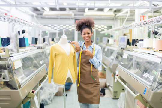 Female designer as a weaver standing pointing at the mannequin Hang a tape measure around your neck. wear uniform There is a thread and the machine is working. in the sewing industry