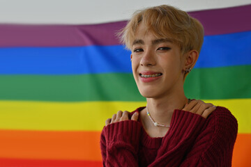 Portrait with Young LGBT teenage boy hugging himself and happily smiling, pride flag on the background, Hug of self love, Butterfly Hug.