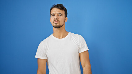 Young hispanic man standing with serious expression over isolated blue background