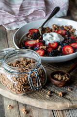 A jar of protein granola clusters with a healthy breakfast bowl in behind.