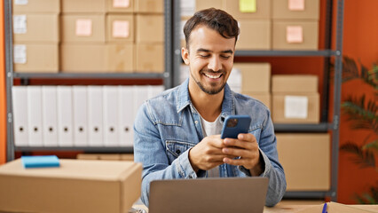 Young hispanic man ecommerce business worker using smartphone smiling at office