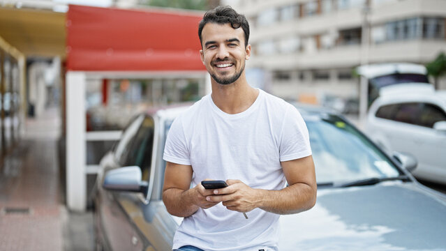 Young hispanic man using smartphone leaning on car at street