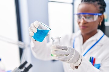 African american woman scientist smiling confident pouring liquid on test tube at laboratory
