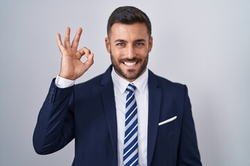 Handsome hispanic man wearing suit and tie smiling positive doing ok sign with hand and fingers. successful expression.