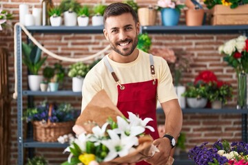 Young hispanic man florist holding bouquet of flowers at florist