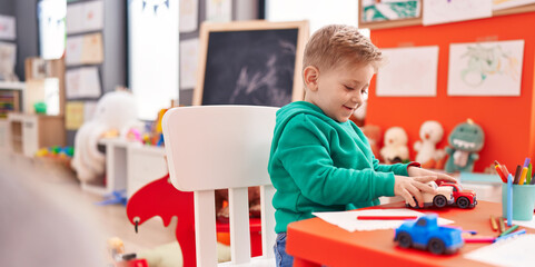 Adorable caucasian boy playing with car toy sitting on table at kindergarten
