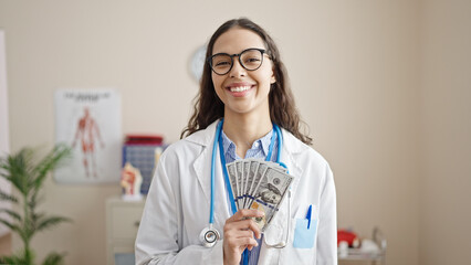 Young beautiful hispanic woman doctor smiling holding money at clinic