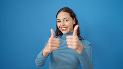Young beautiful hispanic woman smiling with thumbs up over isolated blue background
