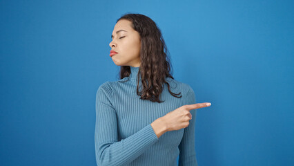 Young beautiful hispanic woman pointing to blank space with angry face over isolated blue background