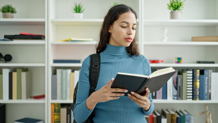 Young beautiful hispanic woman student standing reading book at university classroom