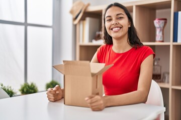 Young brazilian woman looking inside cardboard box with a happy and cool smile on face. lucky...