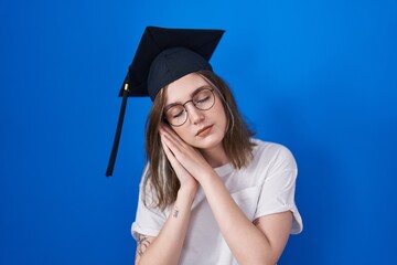 Blonde caucasian woman wearing graduation cap sleeping tired dreaming and posing with hands together while smiling with closed eyes.