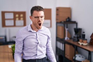 Young hispanic man at the office angry and mad screaming frustrated and furious, shouting with anger. rage and aggressive concept.