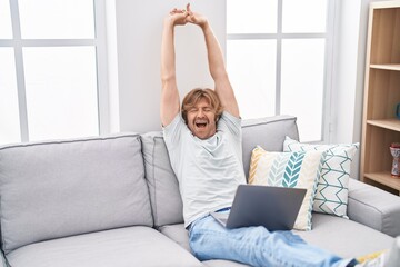 Young man using laptop stretching arms and yawning at home