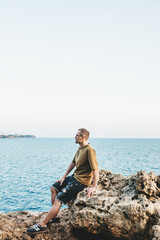 Naklejka na ściany i meble A young guy is sitting on the seashore and enjoying the sunset