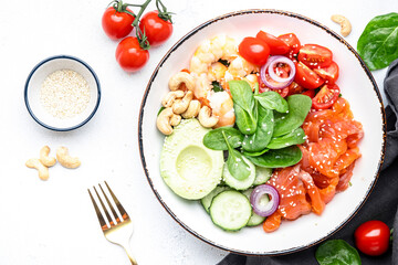 Keto salad with spinach, salmon, shrimp, avocado, cucumber, tomato, nuts, sesame seeds. Low-carbohydrate lunch rich in healthy fats. White table background, top view