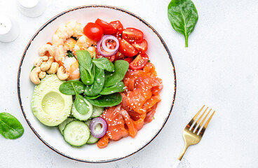 Keto salad with spinach, salmon, shrimp, avocado, cucumber, tomato, nuts, sesame seeds. Low-carbohydrate lunch rich in healthy fats. White table background, top view