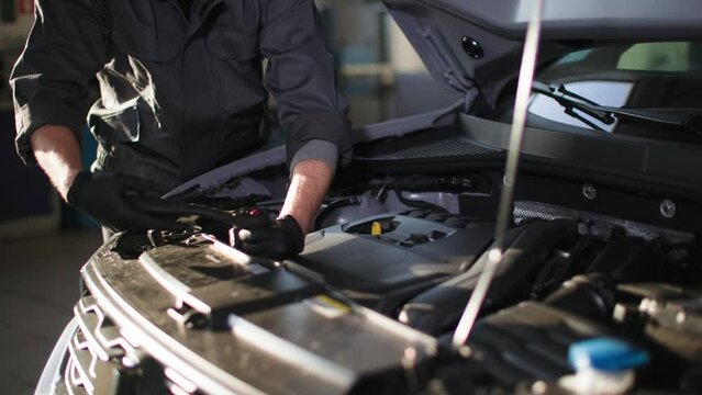 auto maintenance, young man in uniform repairs car engine with wrench backdrop of sun rays, close-up