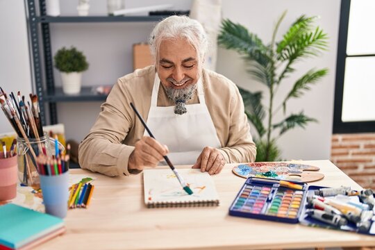 Middle age grey-haired man artist smiling confident drawing on notebook at art studio