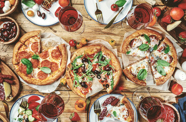 Pizza party table. Top view glasses with red wine, rustic wooden table with hot pizzas, italian...