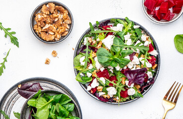 Beetroot and white cheese salad with arugula, lettuce, chard and walnuts, white table, copy space. Fresh useful vegetarian dish for healthy eating