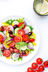 Vegan salad with kalamata olives, cherry tomato, yellow paprika, cucumber and red onion, tasty and healthy mediterranean food, low calories eating. White table background, top view