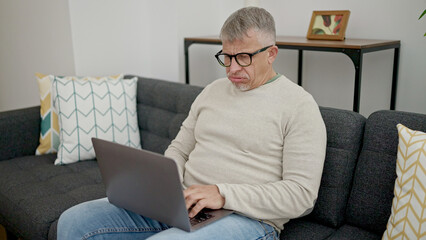 Middle age grey-haired man using laptop with stressed expression at home