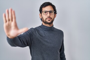 Handsome latin man standing over isolated background doing stop sing with palm of the hand. warning expression with negative and serious gesture on the face.