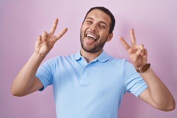 Fototapeta premium Hispanic man standing over pink background smiling with tongue out showing fingers of both hands doing victory sign. number two.