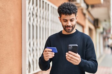 Young arab man using smartphone and credit card at street