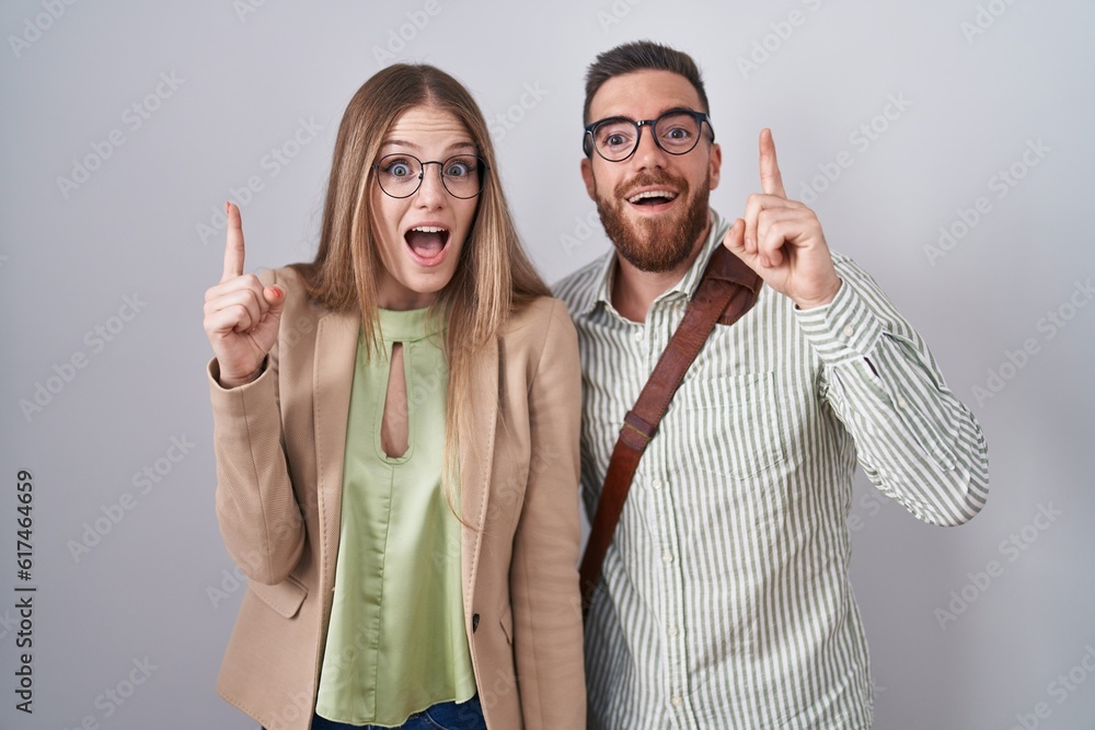 Wall mural Young couple standing over white background pointing finger up with successful idea. exited and happy. number one.