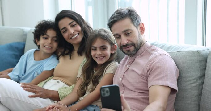 Beautiful smiling multinational family take selfie pictures on smart phone camera, bloggers record video vlog, enjoy new mobile application, having fun using modern tech on carefree leisure at home