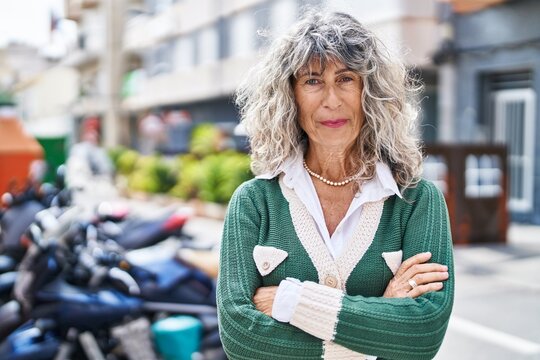 Middle age woman smiling confident standing with arms crossed gesture at street