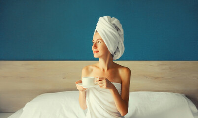 Happy young woman enjoying with cup of coffee drying her wet hair after bath with wrapped towel on...