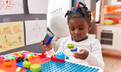 African american girl playing with construction blocks sitting on table at kindergarten