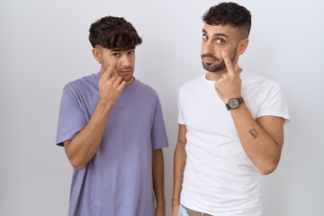 Homosexual gay couple standing over white background pointing to the eye watching you gesture, suspicious expression