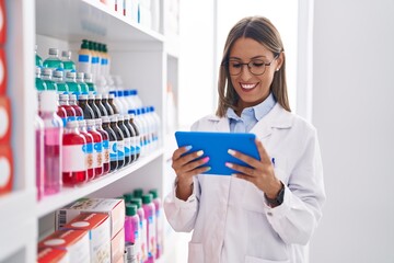 Young beautiful hispanic woman pharmacist using touchpad working at pharmacy