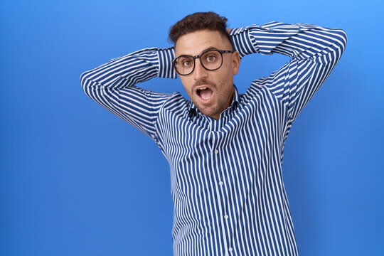 Hispanic man with beard wearing glasses crazy and scared with hands on head, afraid and surprised of shock with open mouth