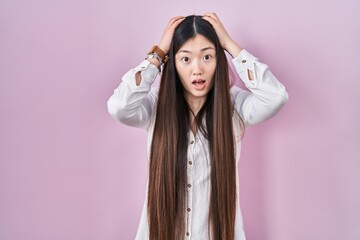 Chinese young woman standing over pink background crazy and scared with hands on head, afraid and surprised of shock with open mouth