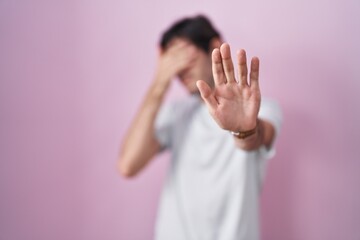 Obraz na płótnie Canvas Young hispanic man standing over pink background covering eyes with hands and doing stop gesture with sad and fear expression. embarrassed and negative concept.