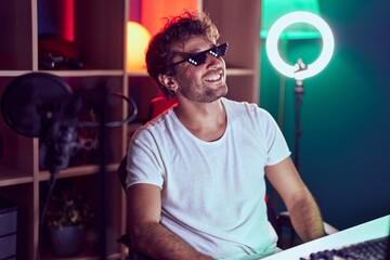 Young hispanic man streamer smiling confidetn wearing thug life glasses at music studio