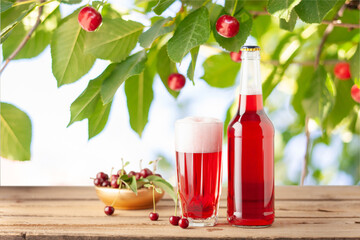 Boozy Refresing Cold Hard Cherry Cider in a Pint Glass and Bottle on wooden table. Copy space